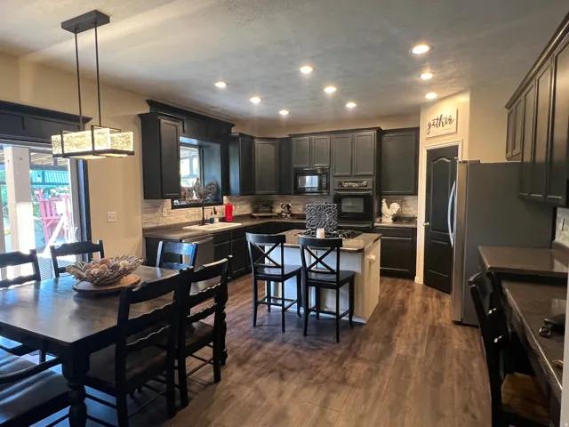 Spacious kitchen featuring dark cabinetry, stainless steel appliances, a center island with bar seating, and wood-finish flooring