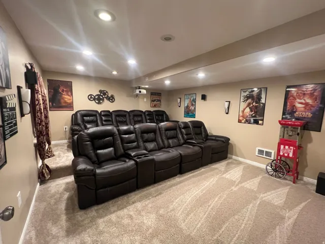 Dedicated media room featuring tiered seating, recessed ceiling lighting, wall-mounted speakers, and a ceiling-mounted projector