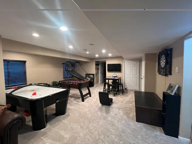 Finished lower level featuring recessed lighting, plush carpeting, a built-in television mount, and multiple windows with horizontal blinds