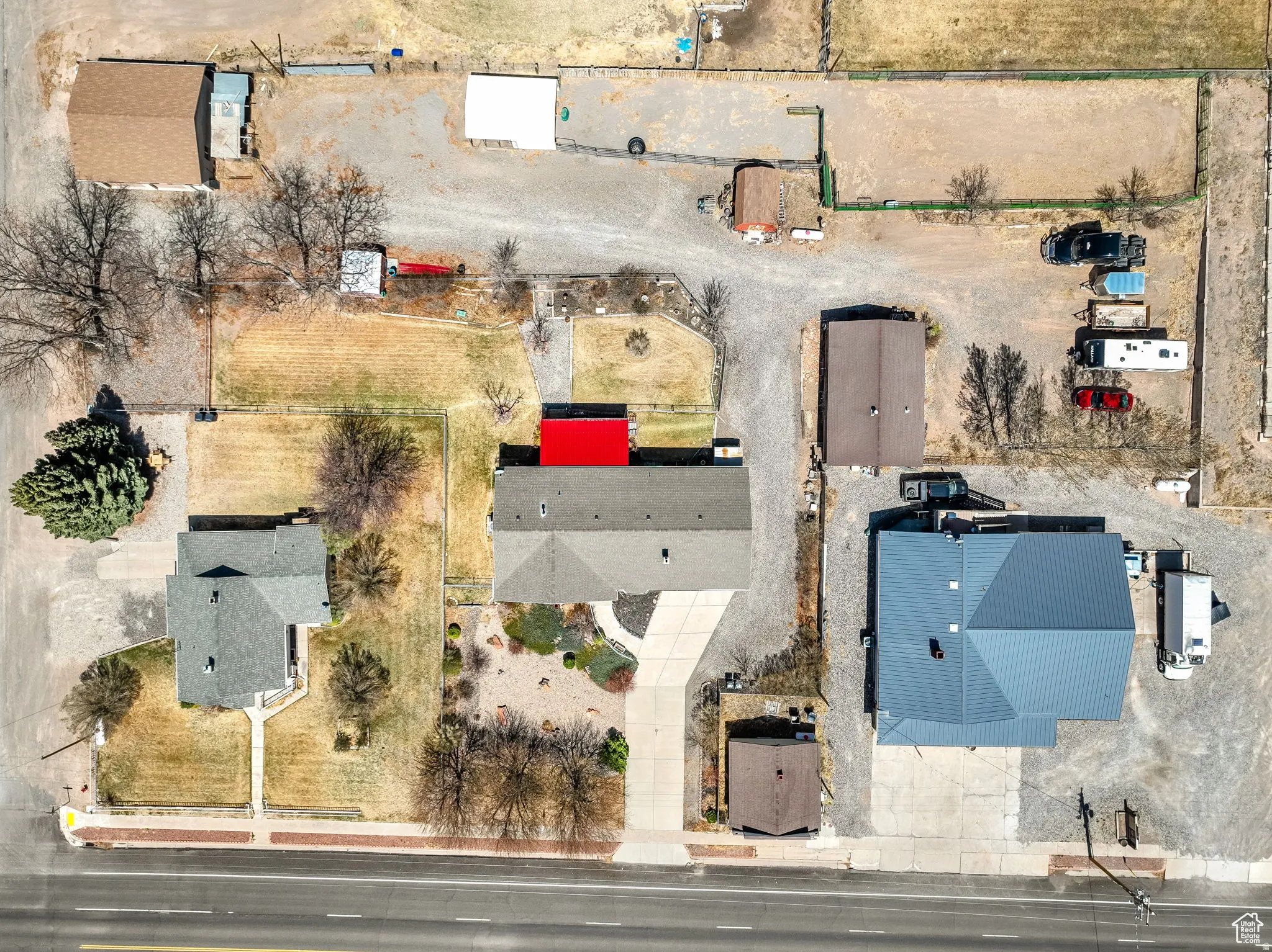 Expansive property featuring three distinct structures with shingle and metal roofing, multiple gravel parking areas, and a paved driveway