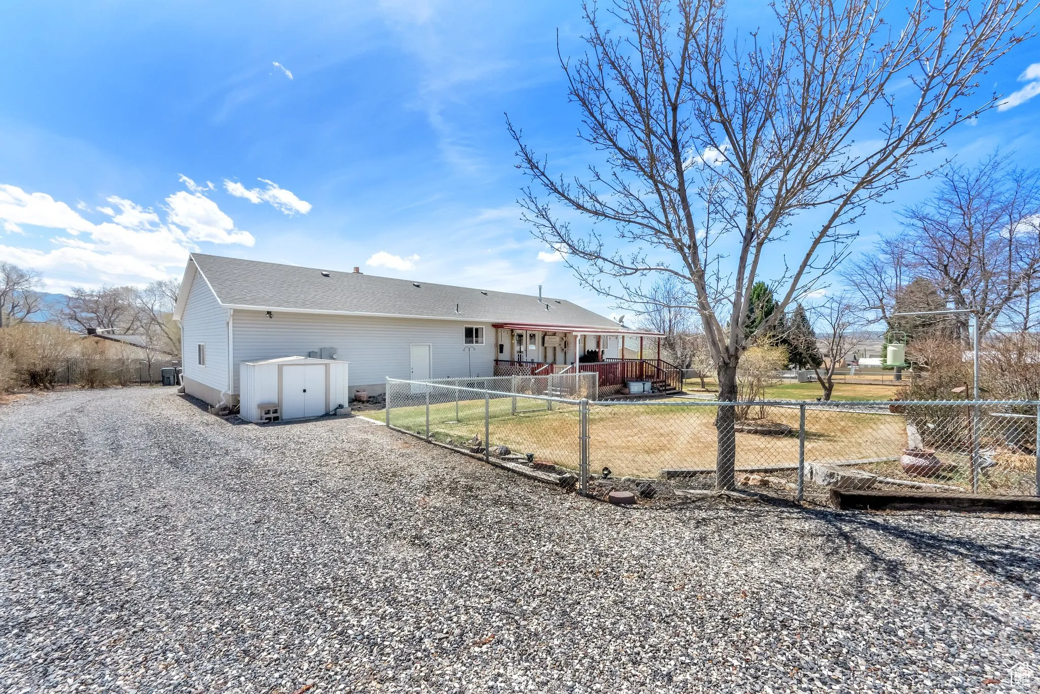 Spacious gravel driveway with a chain-link fence enclosing a backyard area