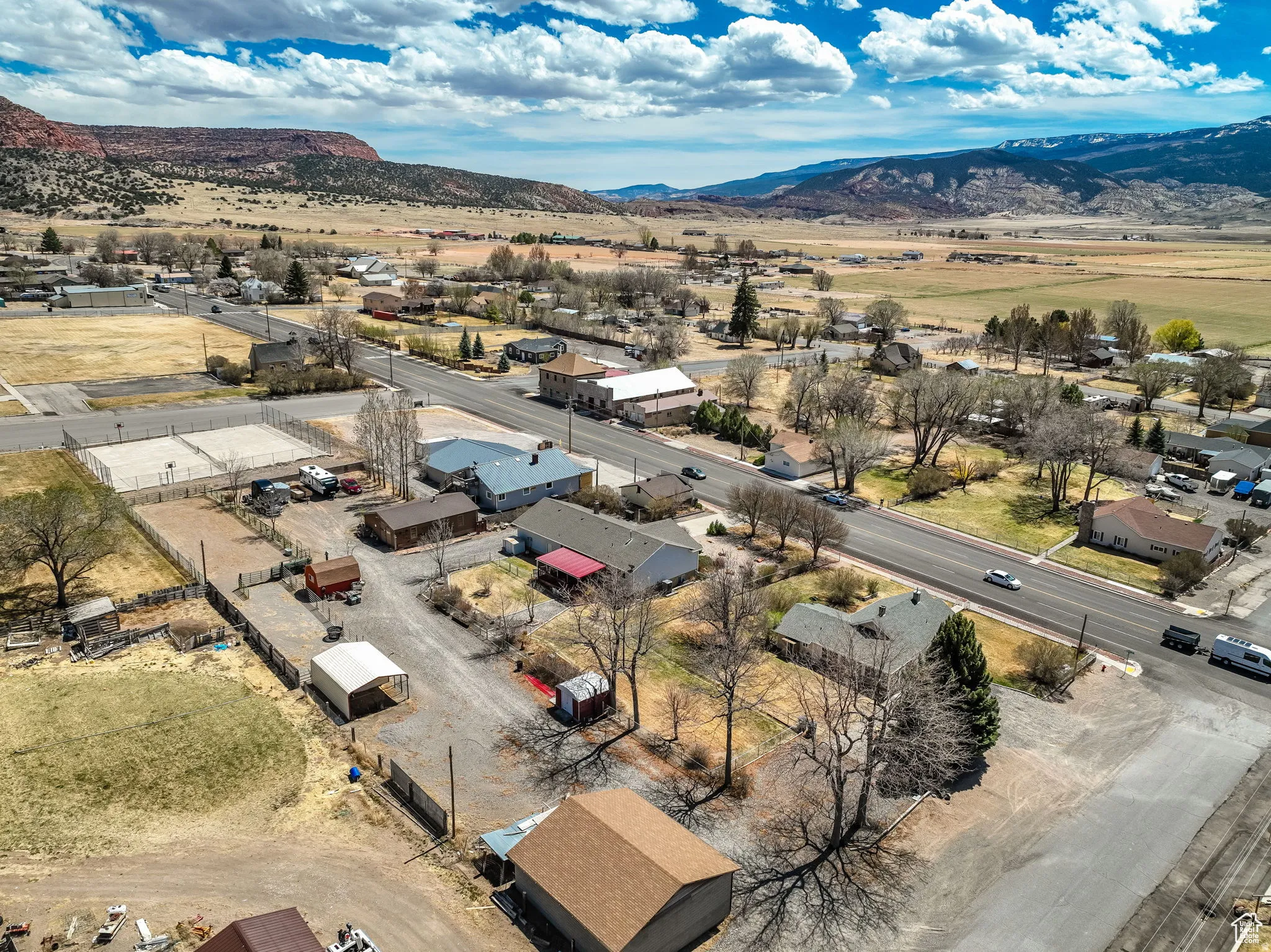 Aerial perspective showcasing a community with varied residential and commercial structures, a main thoroughfare, and extensive natural landscapes with distant mountains