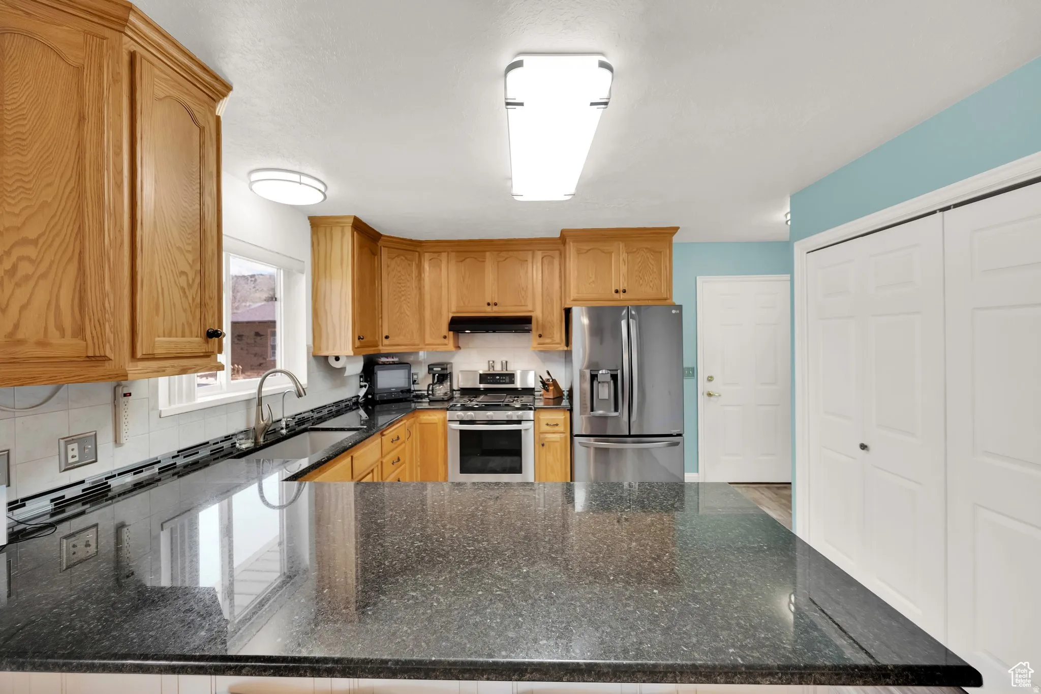 Kitchen featuring wood cabinetry, dark speckled countertops, stainless steel appliances, and a tiled backsplash