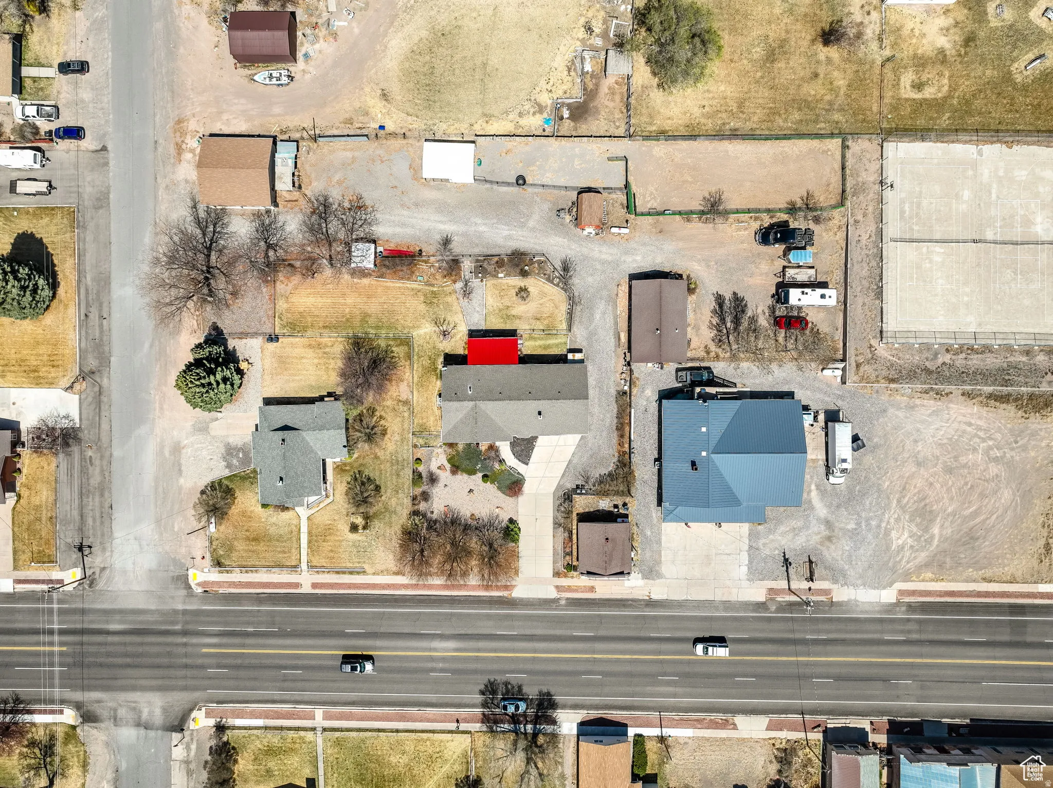 Overhead property view featuring multiple structures, paved road frontage, and extensive gravel areas