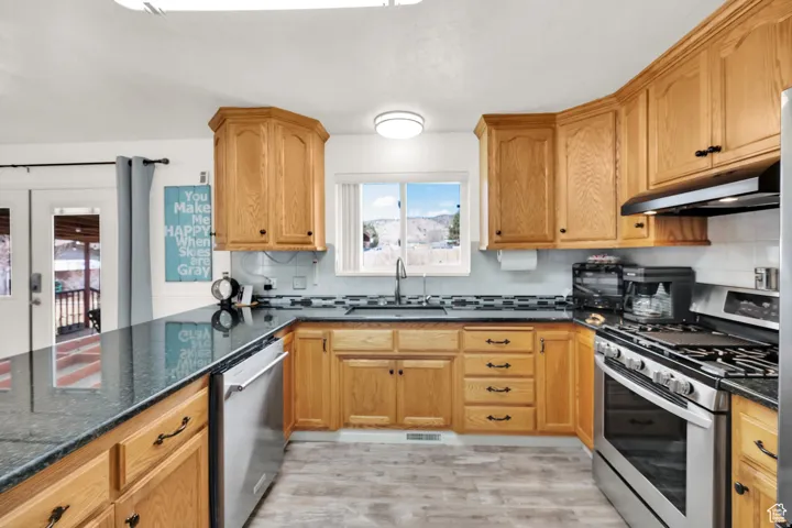 Kitchen featuring abundant wood cabinetry, dark countertops, stainless steel appliances, and a tile backsplash