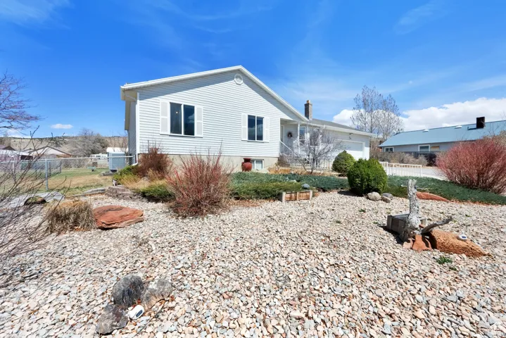 White vinyl siding exterior with an attached garage, featuring a gravel front yard, established shrubs, and decorative rockwork