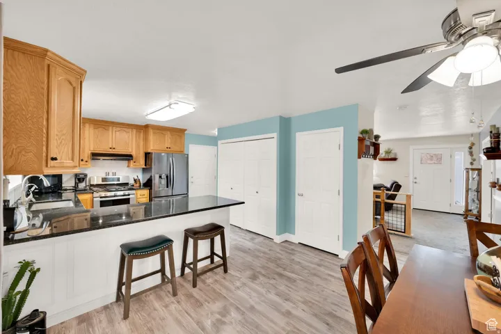 Kitchen featuring wood-finish cabinetry, black stone countertops, stainless steel appliances, and a breakfast bar