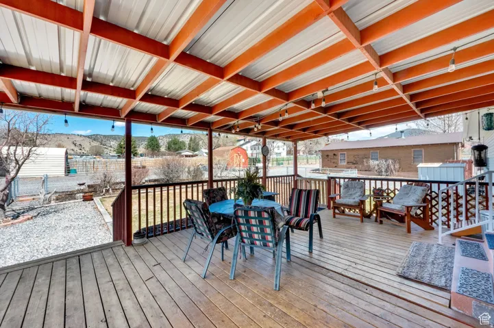 Expansive wood-finish deck featuring a metal-panel overhead cover, exposed wood beams, and string lighting
