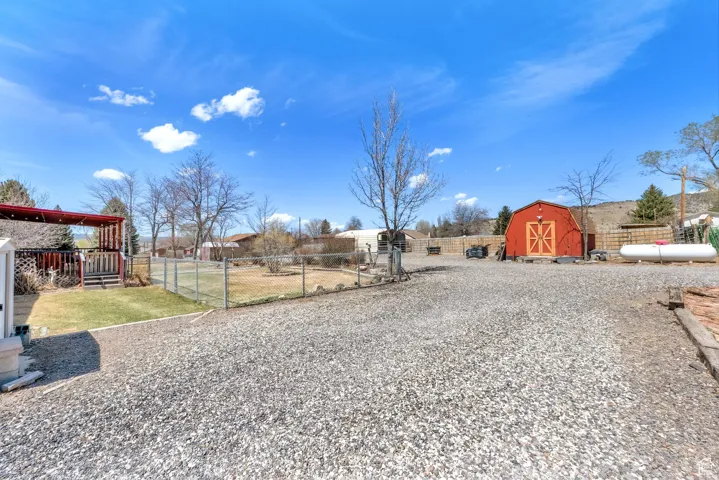Expansive gravel yard featuring a red barn with double doors, fenced green space, and a covered patio area with railing