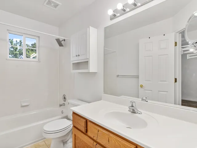 Bright bathroom featuring a wood-finish vanity with dual-sink white countertop, large frameless mirror with integrated lighting, and chrome faucetry