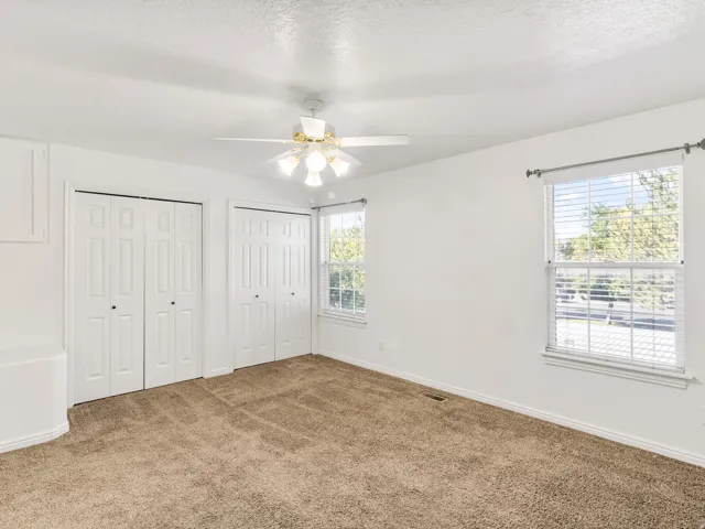 Carpeted room with a ceiling fan, two windows with blinds, and two sets of bi-fold closet doors