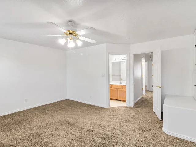 Spacious primary bedroom with neutral wall finishes, plush carpet flooring, and ceiling fan with integrated lighting