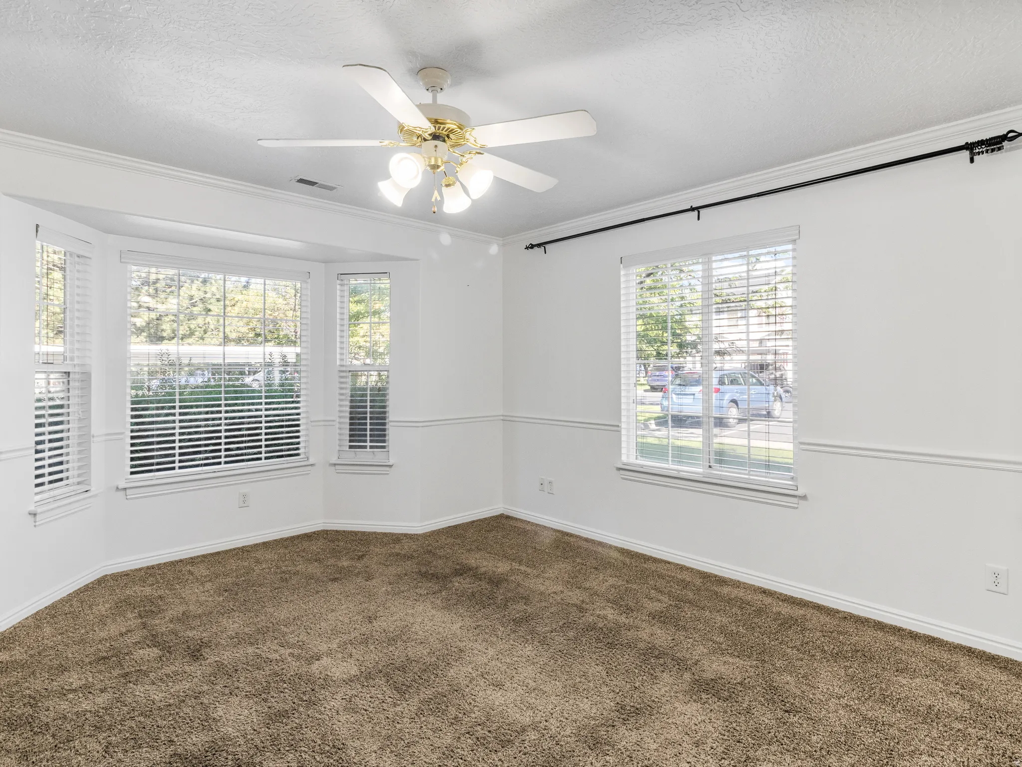 Room featuring a bay window, additional window with white blinds, neutral carpeting, and a ceiling fan with integrated lighting
