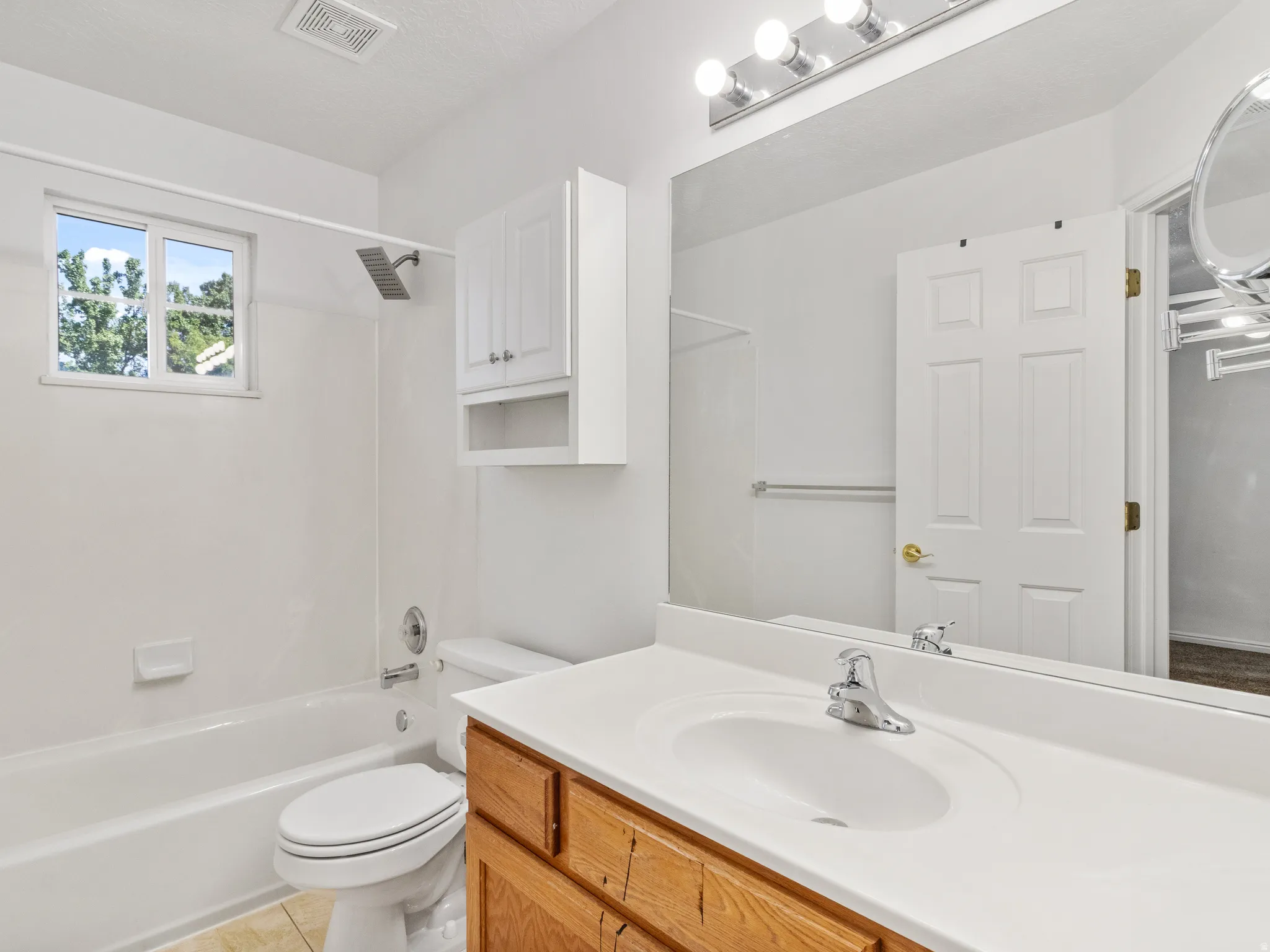 Bathroom featuring a wood-finish vanity with an integrated sink, a large wall-mounted mirror, and overhead vanity lighting