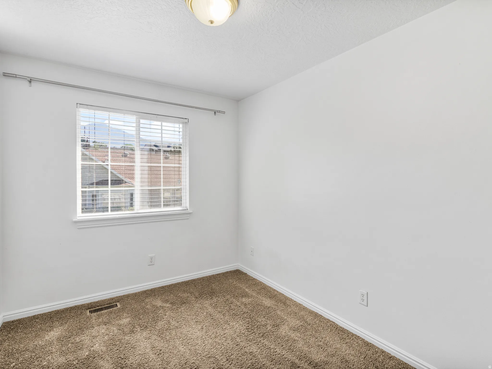Bright room featuring a single window with horizontal blinds, neutral wall paint, and brown carpet flooring