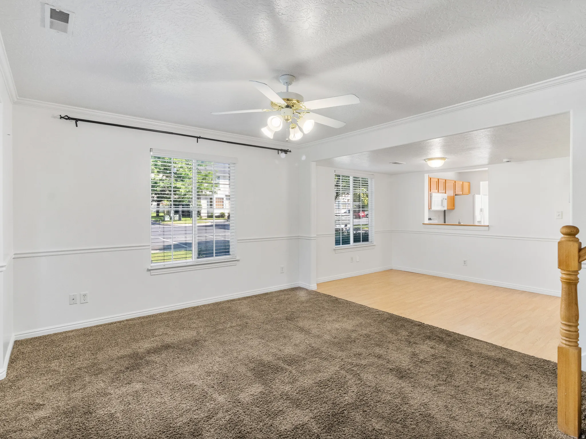Carpeted room featuring a ceiling fan, crown molding, and wainscoting