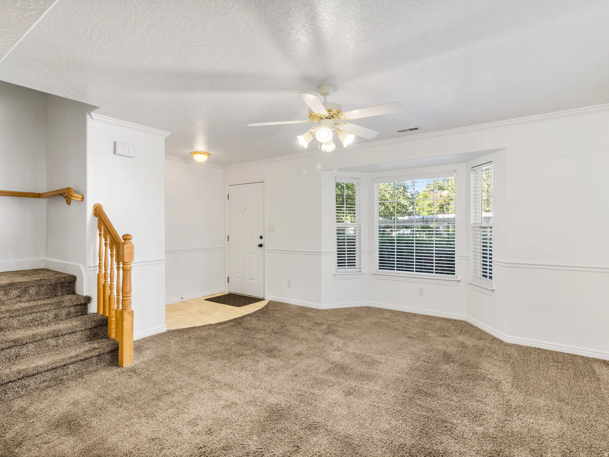 Carpeted living area featuring a bay window with blinds, a ceiling fan, and white trim molding