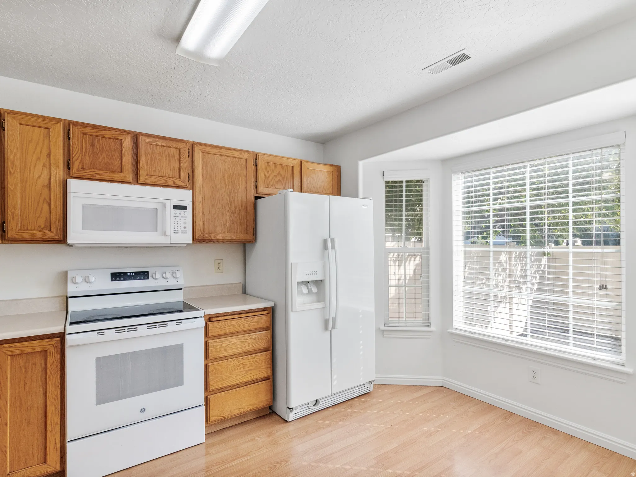 Kitchen featuring wood-finish cabinetry, light countertops, wood-finish flooring, and a bay window area