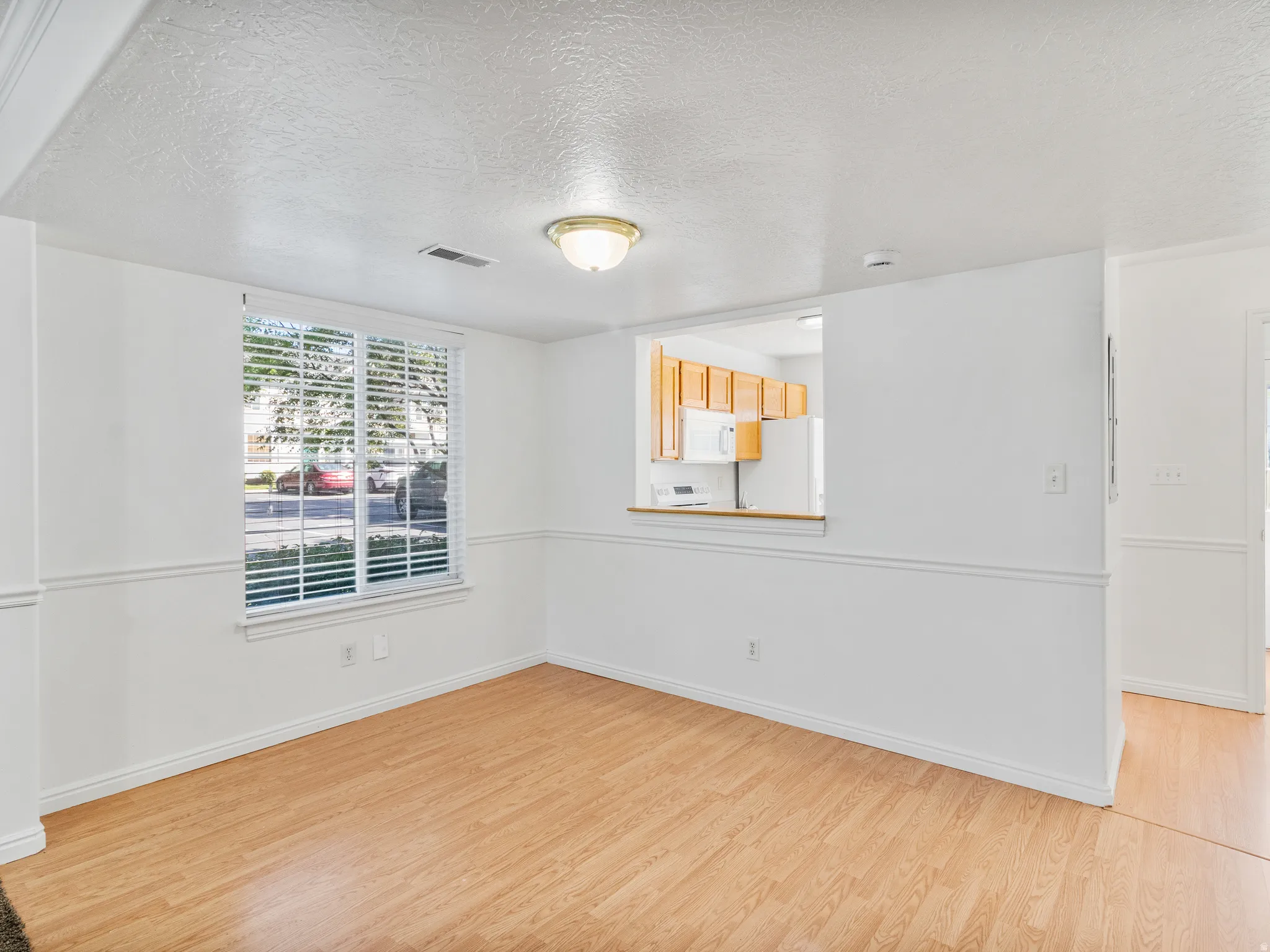 Open concept living space featuring wood-finish flooring, white wainscoting, and a pass-through to the kitchen with wood cabinetry and white appliances