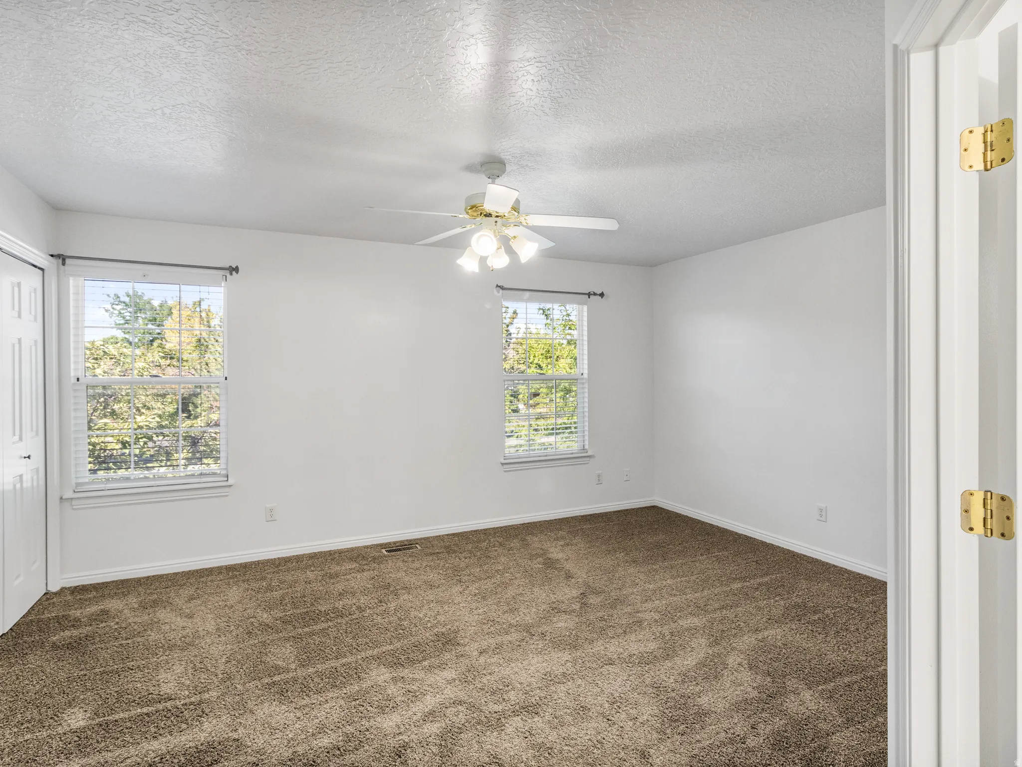 Spacious room featuring neutral carpeting, white walls, and a ceiling fan with integrated lighting