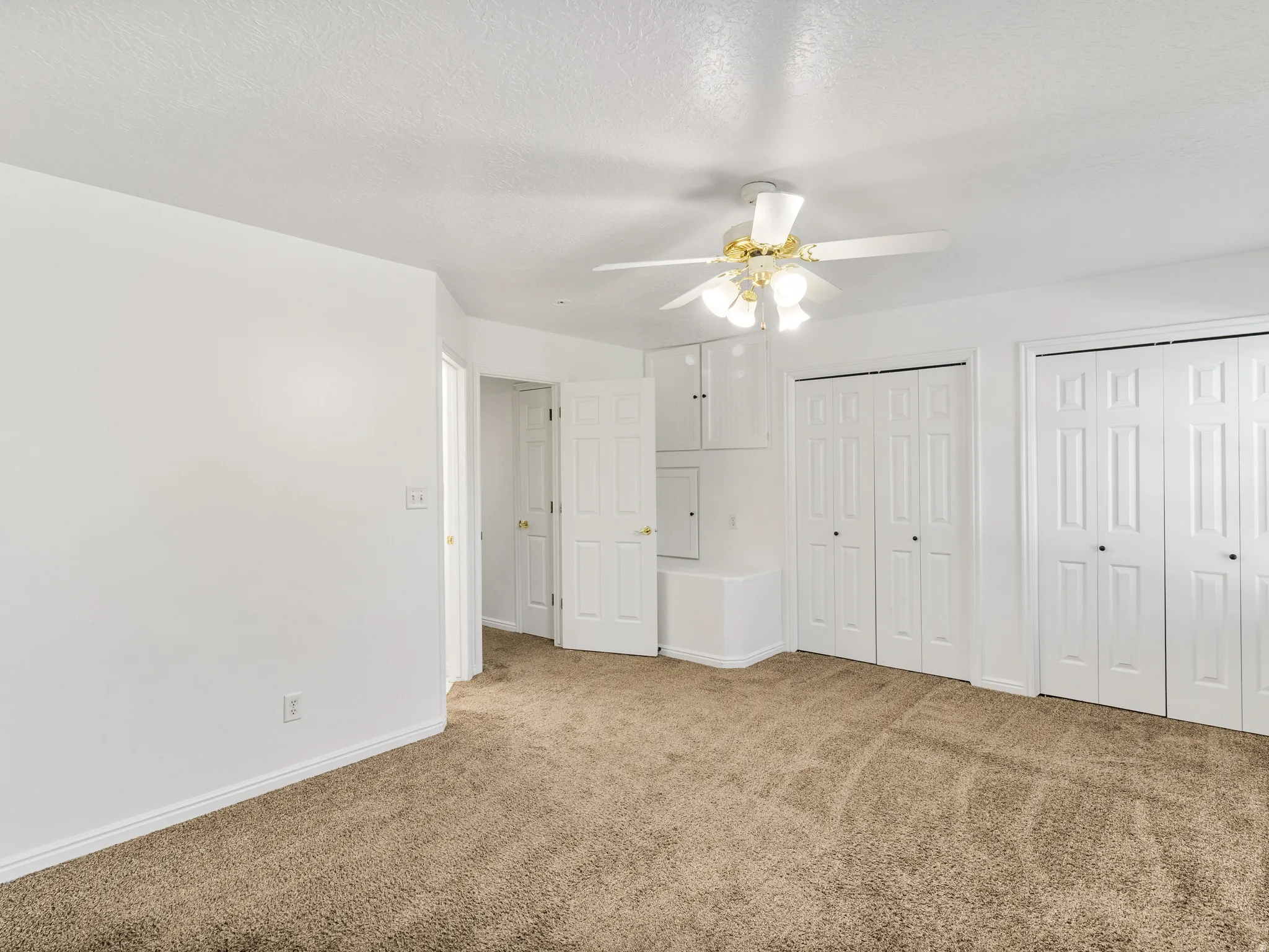 Carpeted room featuring multiple bi-fold closet doors, built-in cabinetry, and a ceiling fan
