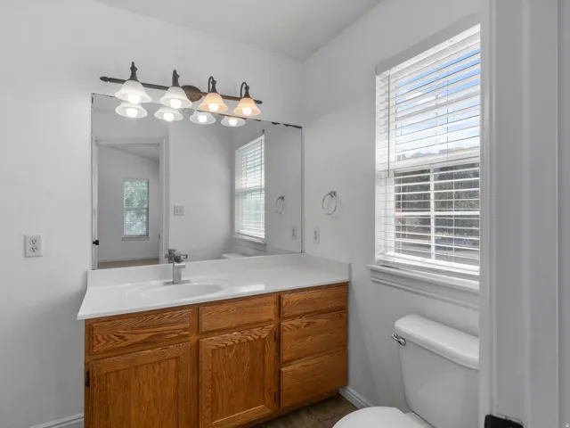 Bathroom featuring a wood-finish vanity with an integrated sink, a vanity mirror, and a window with blinds