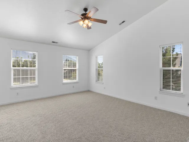 Vaulted ceiling with a ceiling fan, three windows, and neutral carpeting