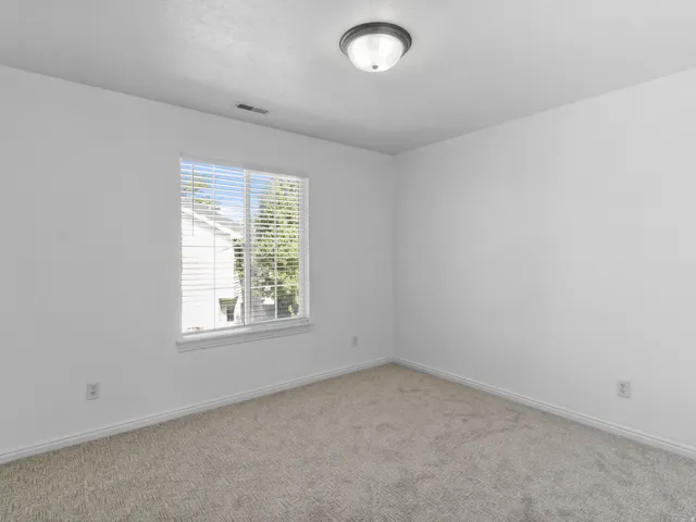 Bright secondary bedroom featuring neutral carpet flooring, abundant natural light from a large window with blinds, recessed ceiling lighting, and fresh white wall finishes