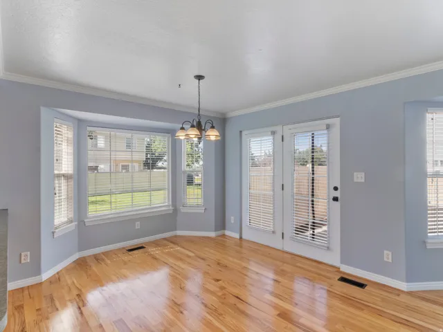 Bright corner living space featuring gleaming wood-finish flooring, soft blue-gray wall finishes, and abundant natural light from multi-pane windows and glass doors with integrated shutters