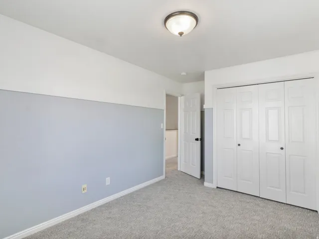 Neutral-toned carpeting, two-tone wall paint, a white paneled door, and bi-fold closet doors with black hardware