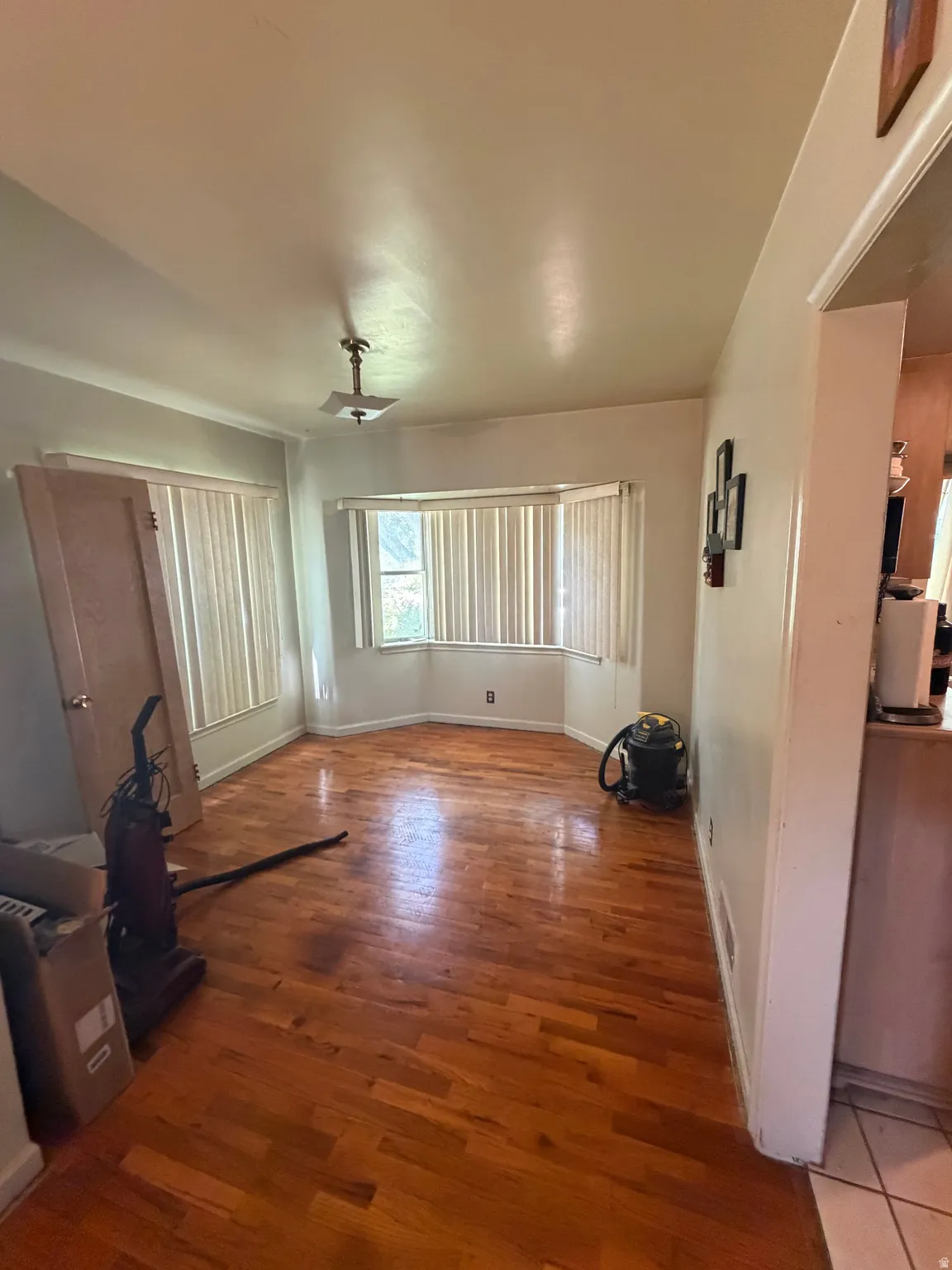 Open-concept room featuring wood-finish flooring, a bay window with blinds, and an overhead light fixture