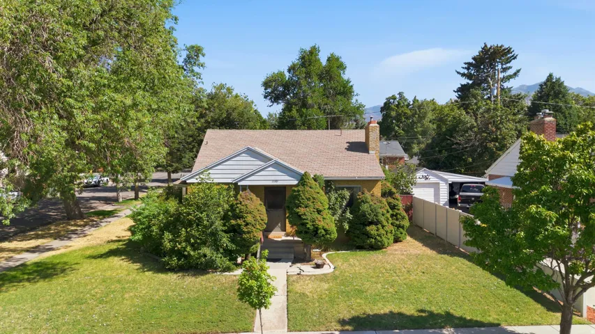 Cottage-style residence featuring a prominent front gable, a mature front yard with established trees, and a concrete pathway leading to the entry