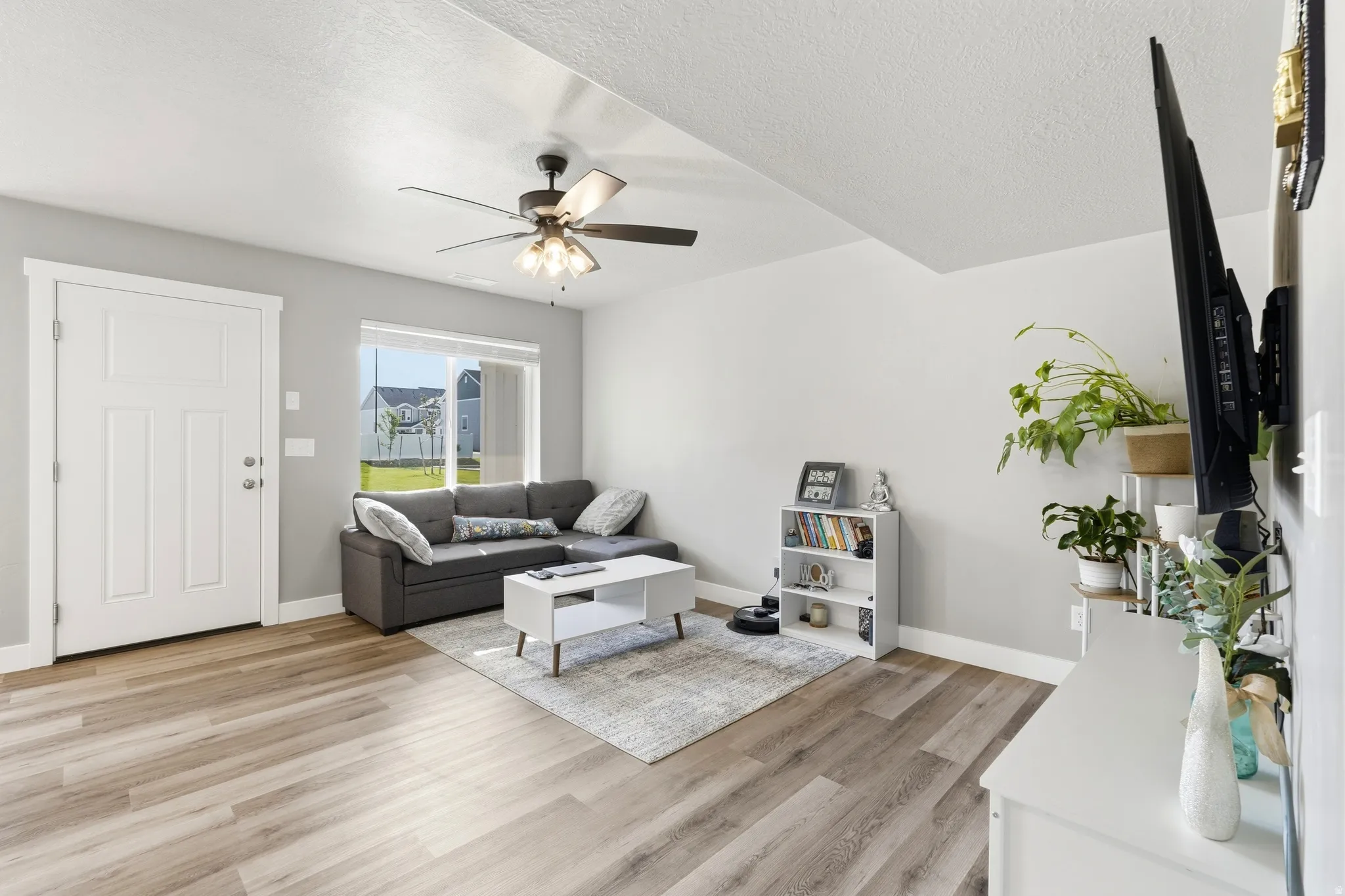 Light-filled living area featuring wood-finish flooring, a contemporary ceiling fan, and large windows with privacy blinds