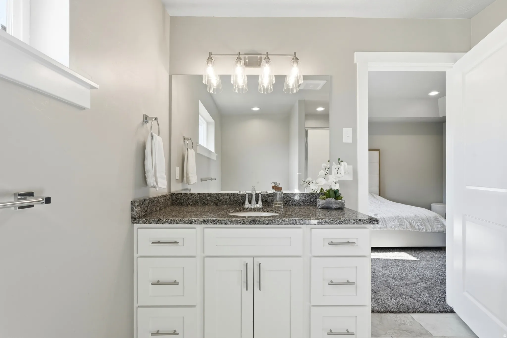 White vanity with brushed nickel hardware, a speckled stone countertop, and an undermount sink