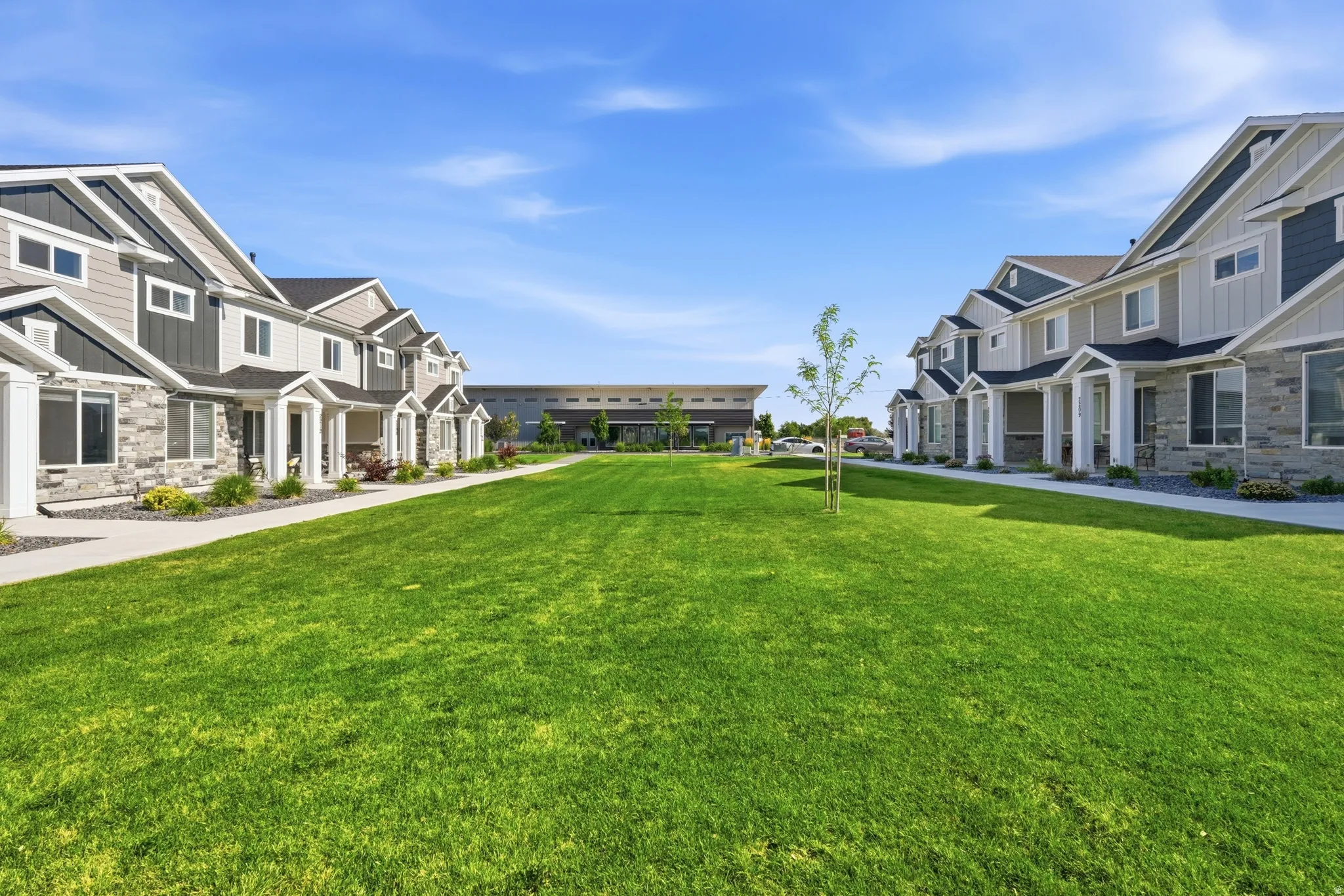 Expansive central green space with a manicured lawn, flanked by a row of townhomes featuring stone and siding exteriors, covered entryways, and white trim accents