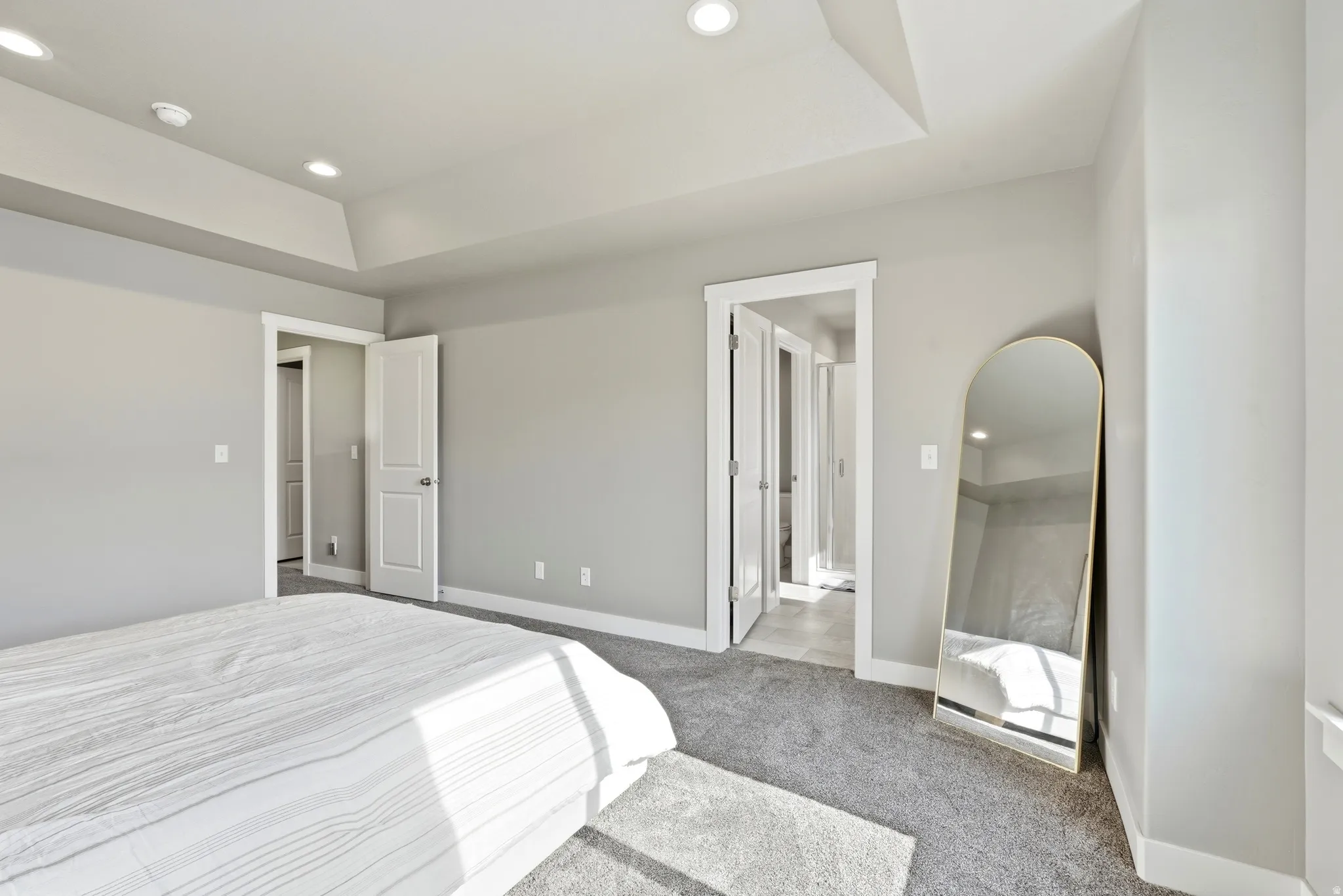 Spacious bedroom featuring light gray walls, plush gray carpeting, a tray ceiling with recessed lighting, and white trim throughout