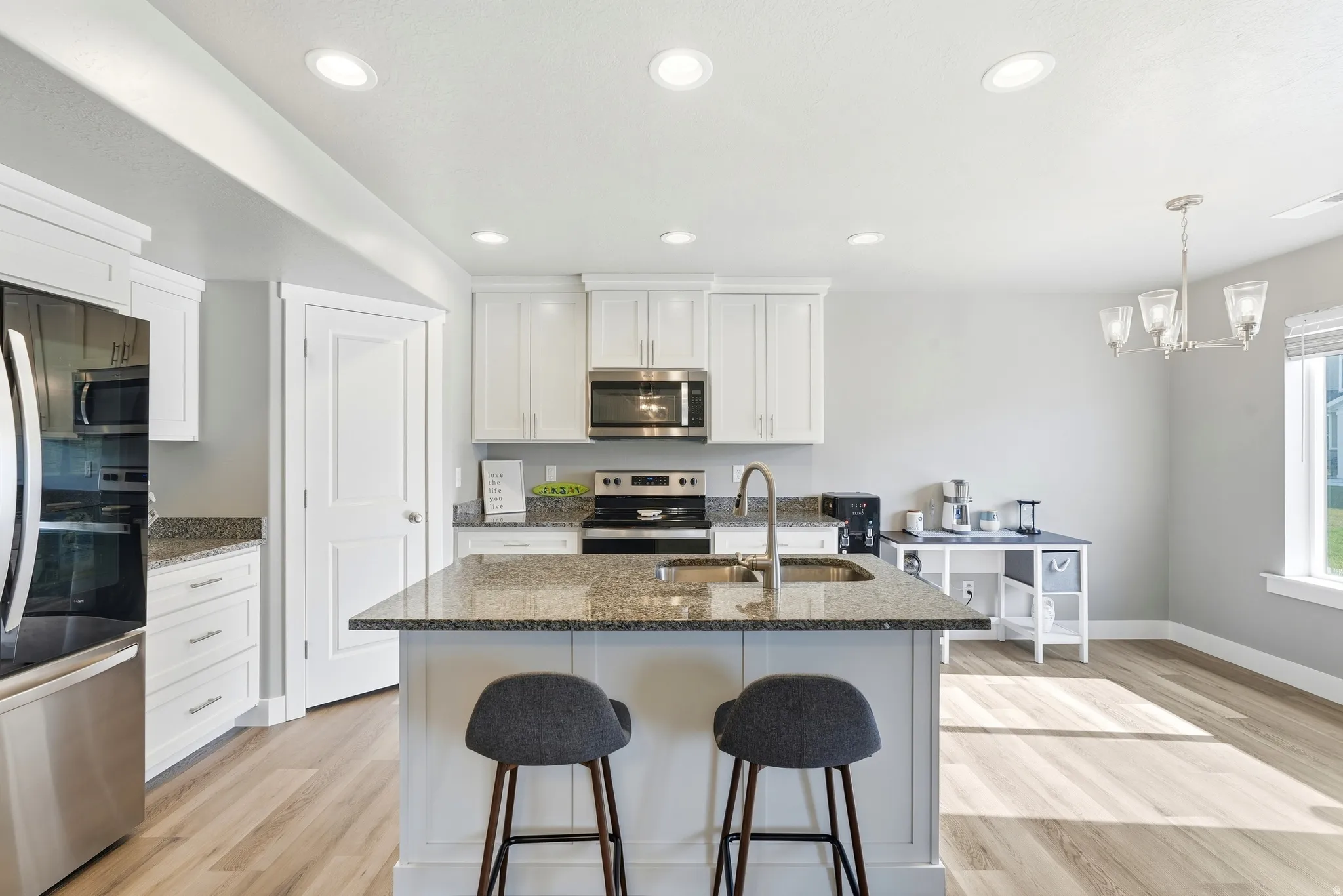 Kitchen featuring a granite-topped island with sink, stainless steel appliances, white cabinetry, recessed lighting, and wood-finish flooring