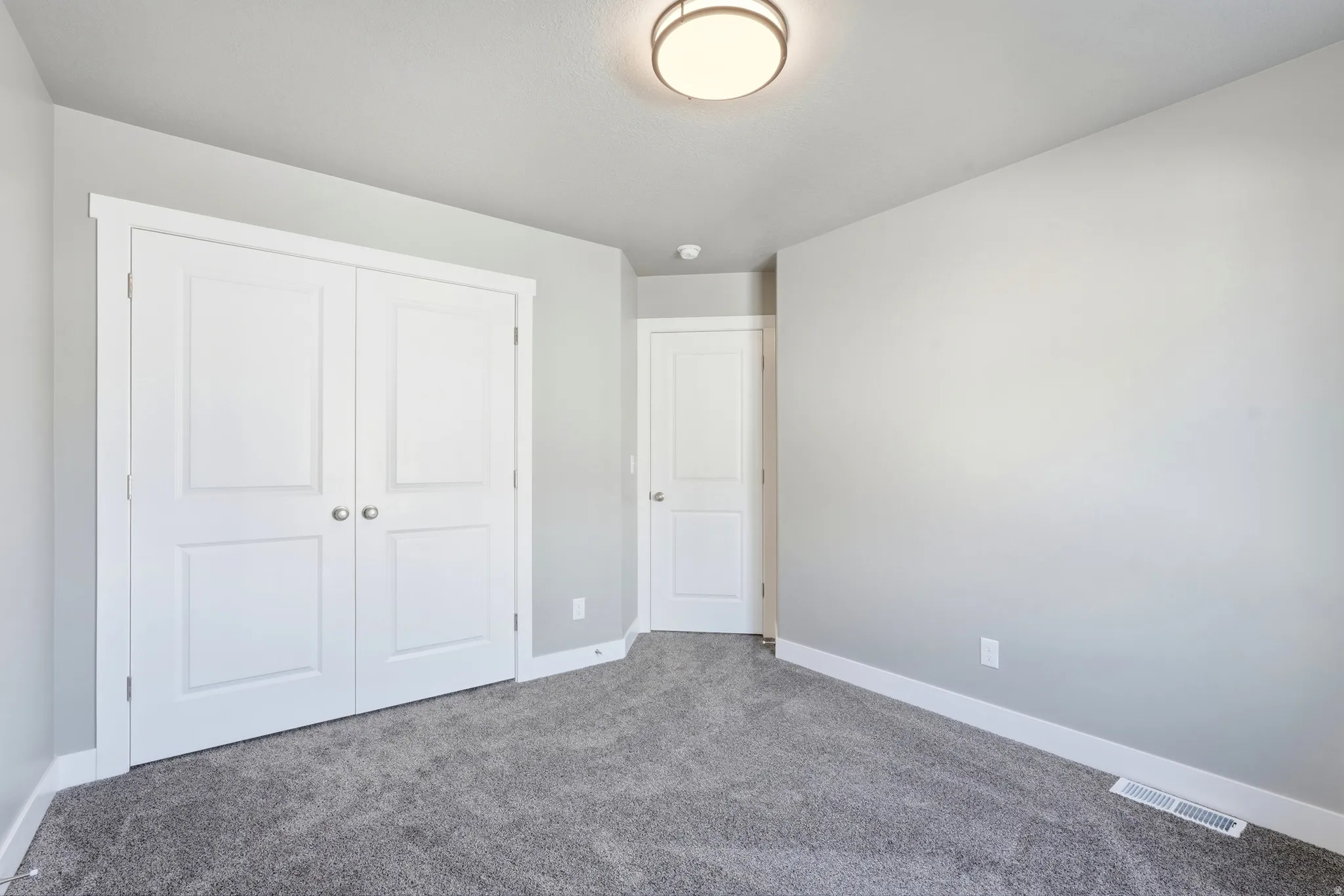 Neutral-toned bedroom featuring plush gray carpeting, white baseboards, and light gray walls