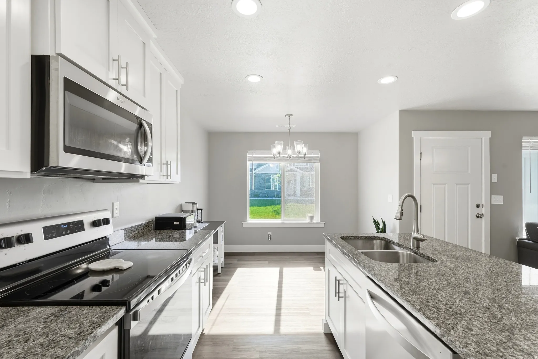Kitchen featuring white cabinetry, stainless steel appliances, granite countertops, an island with an undermount sink, and recessed lighting