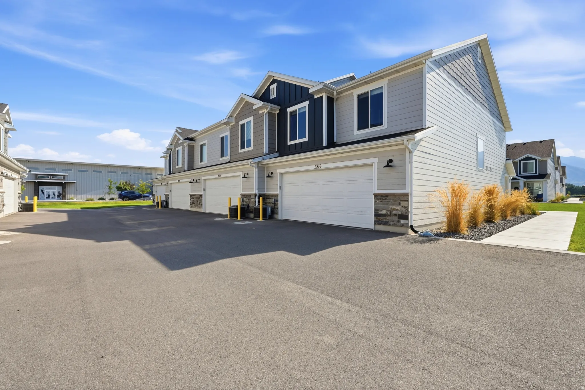 Contemporary townhome exterior featuring light gray siding with dark accent panels, individual garage doors, stone veneer accents, and a paved driveway