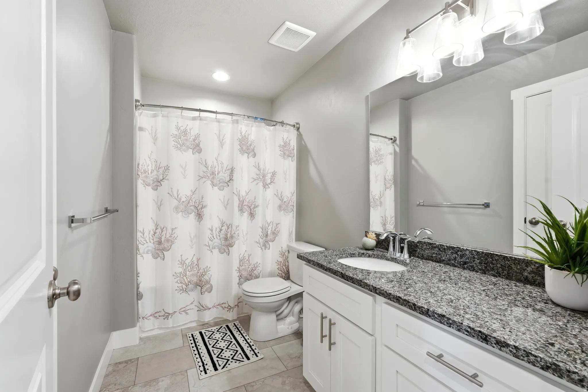 Bathroom featuring a vanity with a dark speckled countertop, white cabinetry, a single basin sink, and a chrome faucet