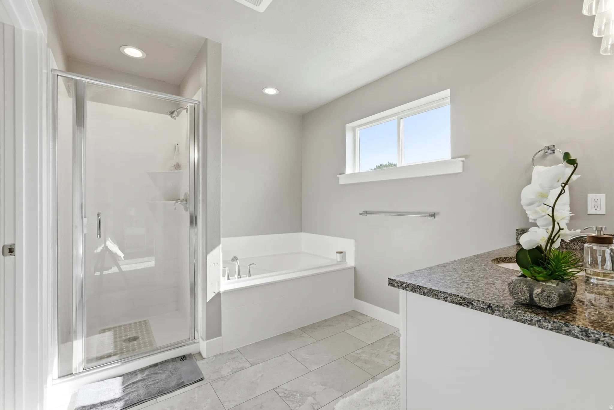 Spacious bathroom featuring a glass-enclosed shower, a large soaking tub, and a vanity with a stone-finish countertop