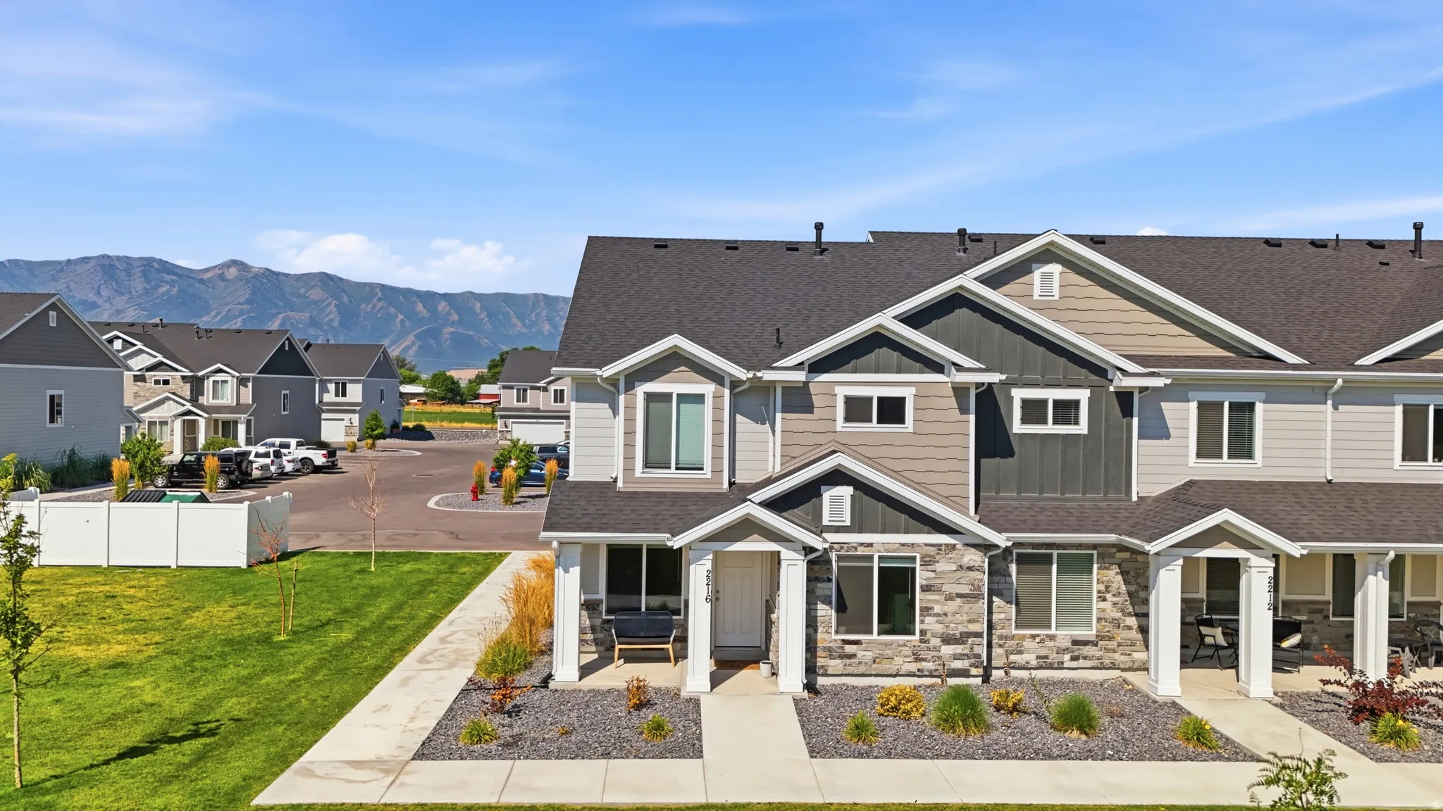 Contemporary townhome featuring a stone and siding facade, covered front porch, dark shingle roof, and an expansive front lawn