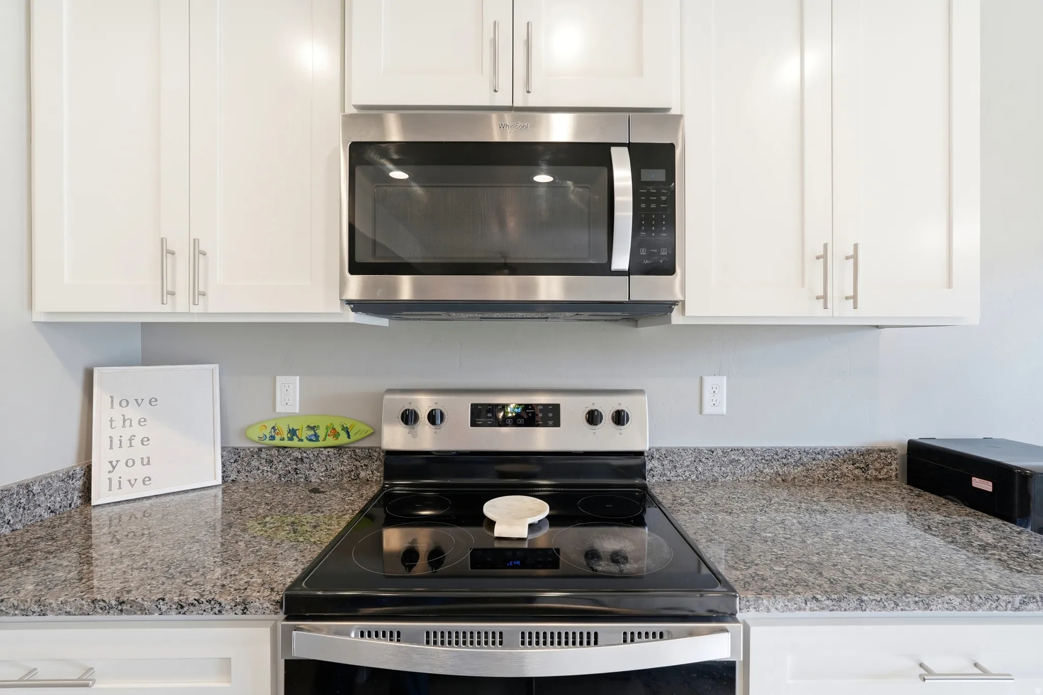 Kitchen showcasing white cabinetry with brushed nickel hardware, stainless steel over-the-range microwave, electric range, and speckled countertops