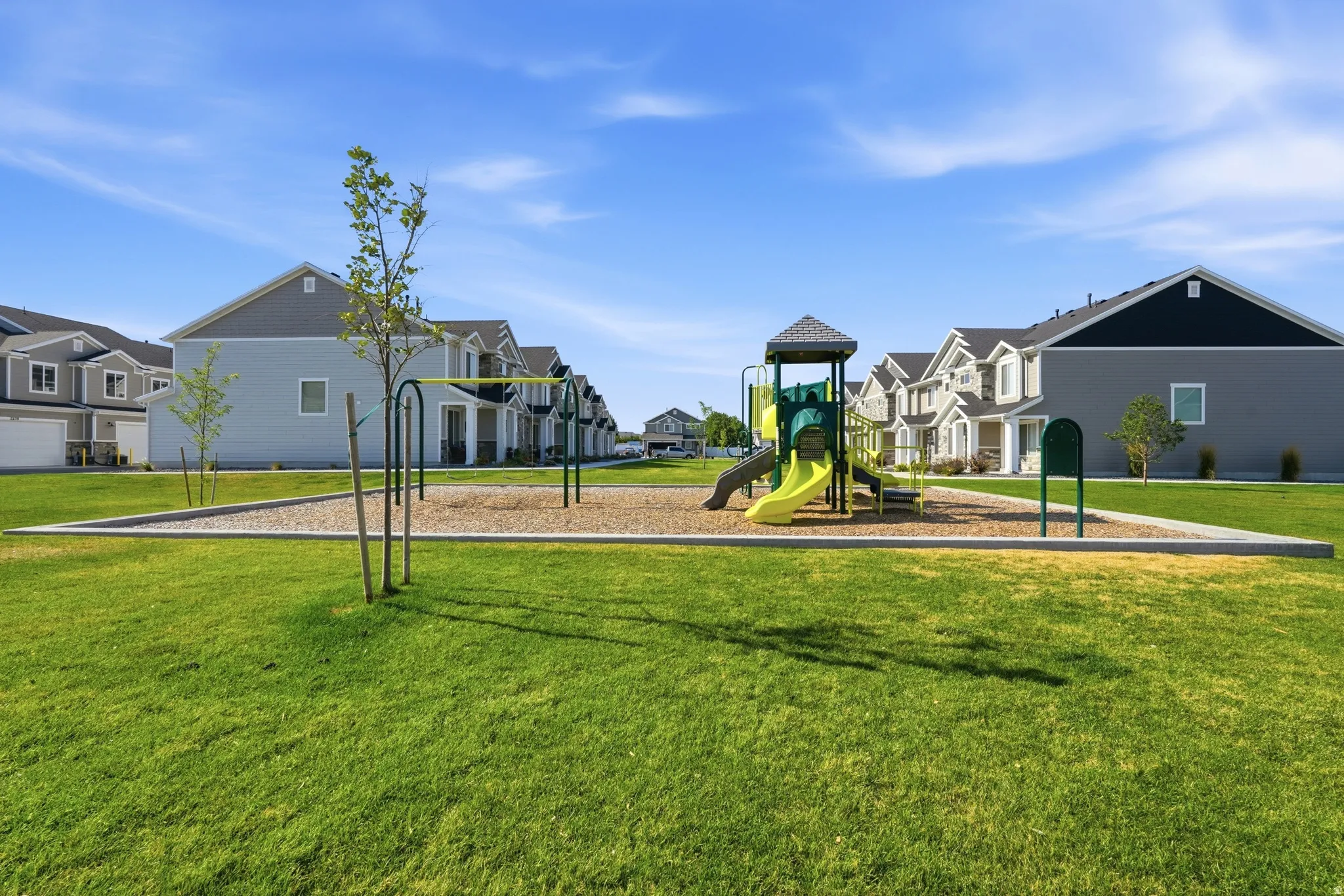 Community green space featuring a playground with slides and swings, surrounded by a manicured lawn
