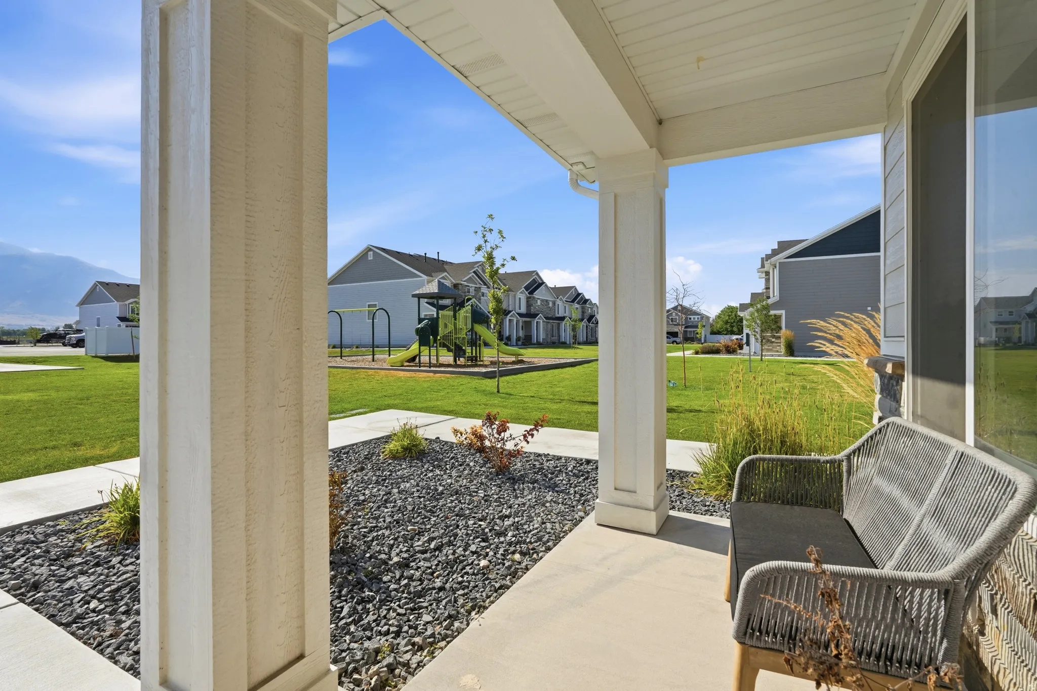 Covered porch entry featuring white columns, a concrete walkway, and decorative rock landscaping