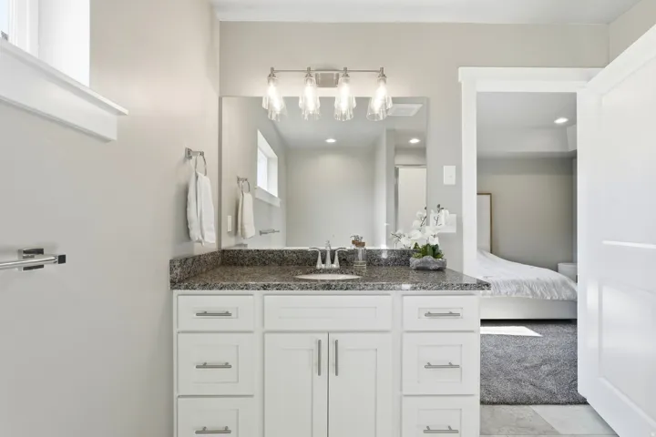 White vanity with brushed nickel hardware, a speckled stone countertop, and an undermount sink
