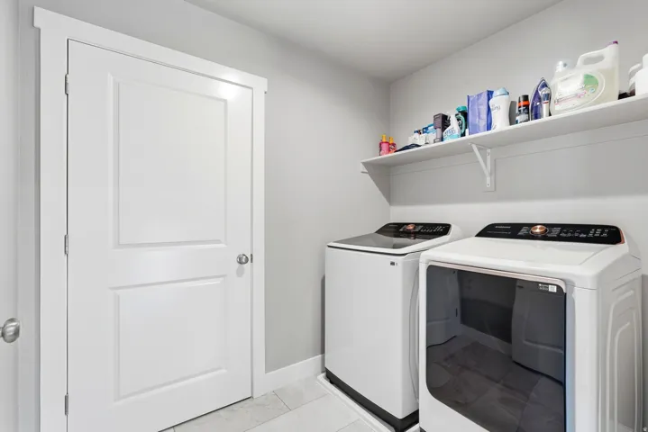Dedicated laundry area featuring a white paneled door, light gray wall paint, tiled flooring, and a long white floating shelf