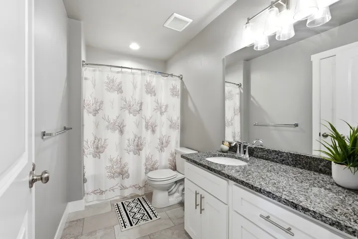 Bathroom featuring a vanity with a dark speckled countertop, white cabinetry, a single basin sink, and a chrome faucet
