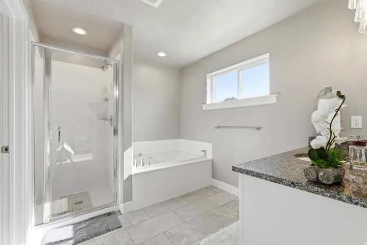Spacious bathroom featuring a glass-enclosed shower, a large soaking tub, and a vanity with a stone-finish countertop
